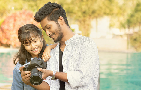 可爱的情侣在相机屏幕上看照片 — 快乐的年轻专业摄影师在他的数码单反相机上展示图像给模特 — 模特和摄影师一起工作的概念。