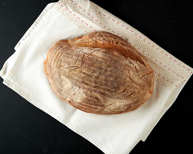 椭圆形的东西摄影照片_黑色木板上的烤椭圆形黑麦面包