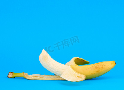 剥香蕉摄影照片_在蓝色背景的被剥皮的成熟黄色香蕉