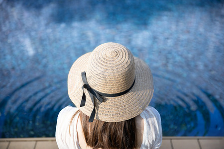 美n摄影照片_身着泳装、头戴草帽的放松女性坐在 n 后的背影