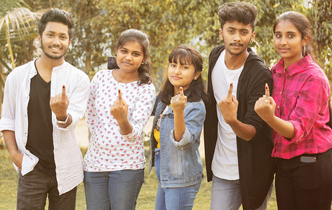 一群青少年朋友在投票后在投票站或亭外展示墨水标记的手指-印度选举或投票系统的概念。