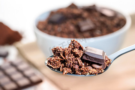 酥脆巧克力摄影照片_勺子用巧克力牛奶什锦早餐和碗在背景中。