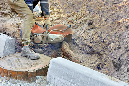 一名工人使用便携式汽油锯清理现场并砍断一棵树的粗壮根部以安装检修孔。