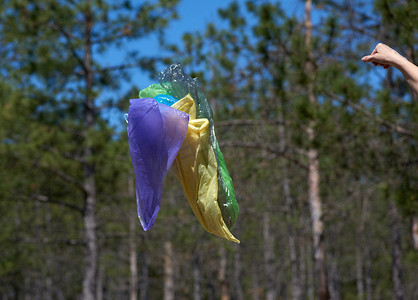 黑色垃圾塑料袋摄影照片_夏日，空垃圾塑料袋在森林中飞舞