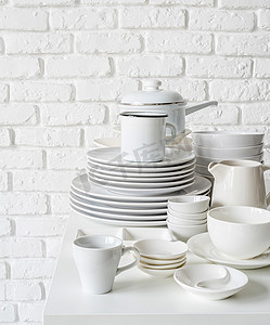 白色砖墙背景的桌子上成堆的白色陶瓷盘子和餐具
