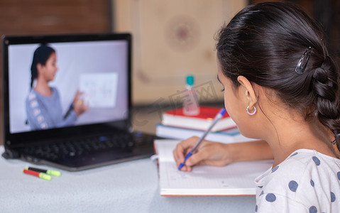 在家上学或电子学习的概念，在 covid-19 或冠状病毒大流行危机期间，年轻女孩忙着看着笔记本电脑写作，而老师则在解释。