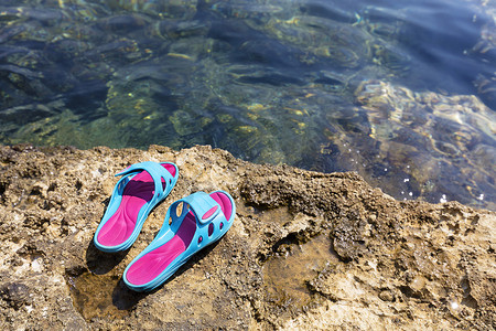 沙滩拖鞋躺在透明大海附近的一块石头上
