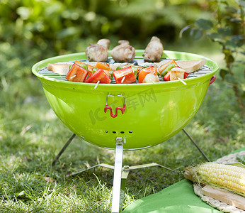 在野餐或夏季露营旅行期间，便携式烧烤架站在带复制空间的绿色草坪上