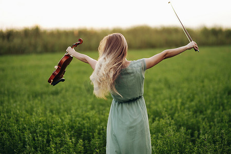 拿小提琴摄影照片_快乐的音乐家小提琴家在夕阳下手里拿着小提琴