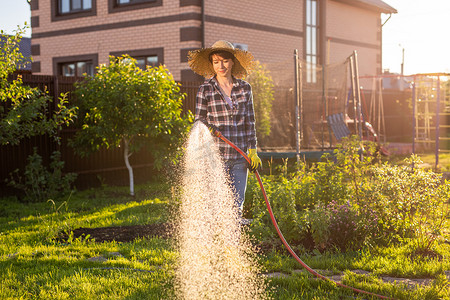 阳光明媚、温暖的夏日，身穿工作服的快乐女园丁在菜园里浇水。