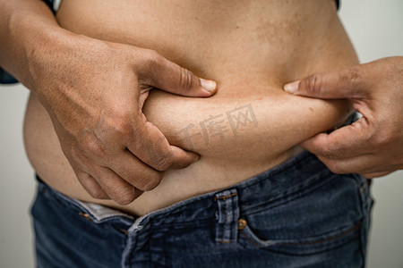 超重的亚洲女性展示并用手挤压肥胖的腹部。
