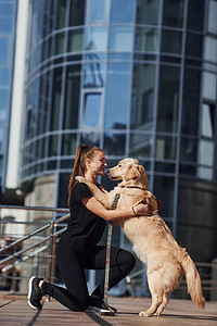 年轻积极的女性在商业大楼附近户外散步时会玩得开心，并与她的狗一起做戏法