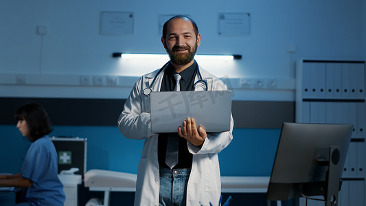 穿着医用白大褂和拿着笔记本电脑的听诊器的微笑全科医生