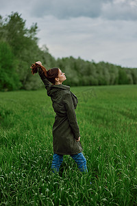 春天雨天，一位身穿深色外套的漂亮女人站在绿色的田野里，拉直头发