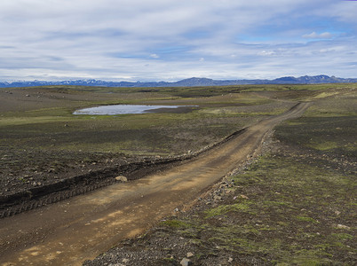中秋月亮云纹摄影照片_冰岛 Fjallabak 自然保护区废弃绿色景观中的土山路，雪覆盖的 rhyolit 山脉，蓝天白云