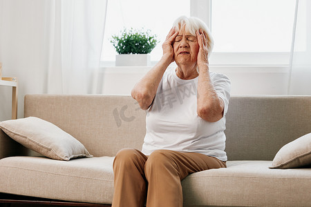 老年妇女坐在沙发上头部剧烈疼痛，老年健康问题，生活质量差。
