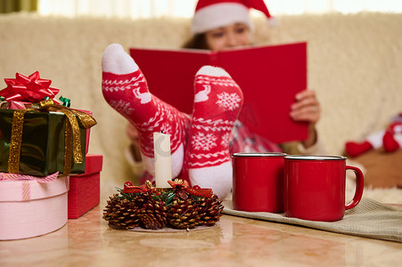 寒假阅读摄影照片_关注带有圣诞图案的红袜子，关注寒假时戴着圣诞帽读书的女性模糊的背景