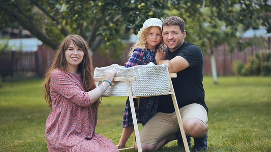 摇摄影照片_一个年轻的家庭看着花园里摇篮里的新生婴儿。
