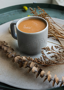 花背景奶茶摄影照片_蓝色陶瓷杯中的热橙奶茶、陶瓷上的甜茶点泰式奶茶和陶瓷盘上的干花。