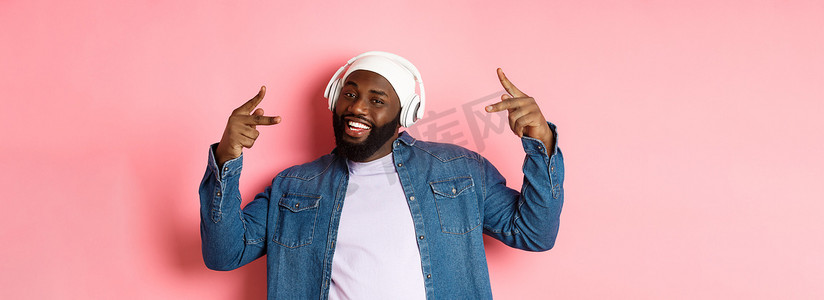 酷炫的非洲裔美国人跳嘻哈舞，戴着耳机听音乐，站在粉红色的背景上
