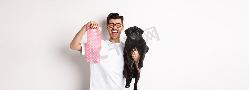 快乐男人、宠物主人的形象，拿着可爱的黑色哈巴狗和狗屎袋，站在白色背景上