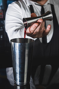 专业调酒师的手将糖浆倒入金属工具中的量杯中，用于制备和搅拌摇酒饮料的酒精鸡尾酒