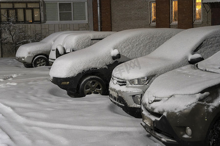 下雪院子里摄影照片_院子里的露天停车场里停满了积雪的汽车