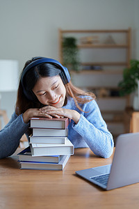 年轻美丽的亚洲女性在清晨在线课堂上微笑的肖像，在家中用书籍、耳机和电脑作为学习材料
