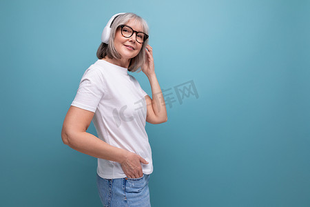 头发灰白的现代成熟女性在工作室背景下用无线耳机听音乐，并有复制空间