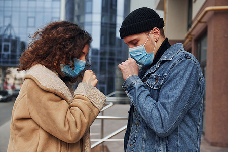 呼吸隔离摄影照片_隔离期间，一对戴着防护口罩的夫妇在城市商业大楼附近的户外咳嗽。