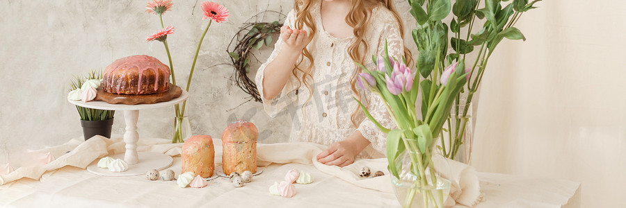 长发连衣裙女孩摄影照片_一个穿着浅色连衣裙、长发的女孩坐在复活节餐桌旁，桌上摆着蛋糕、春天的花朵和鹌鹑蛋。