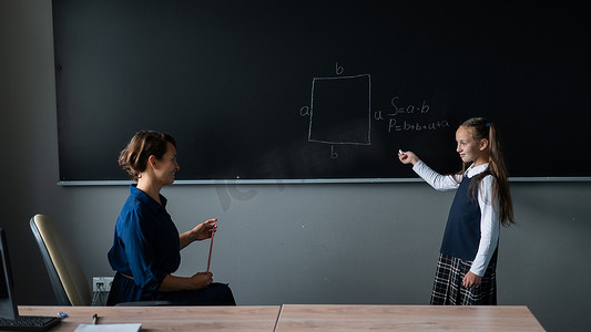白人小女孩在黑板上回答女老师的问题。
