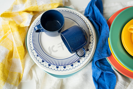 色彩餐具摄影照片_餐桌上摆放着不同尺寸和颜色的色彩鲜艳的碗、盘子和杯子，呈金字塔形。