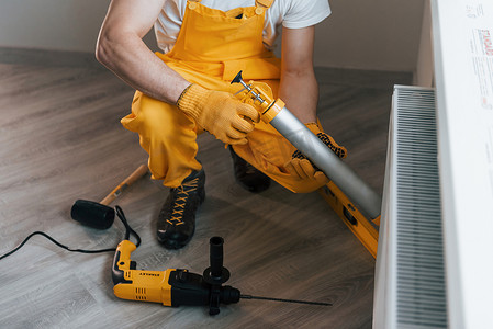 家杂摄影照片_身穿黄色制服的杂工使用特殊工具在室内用热电池工作。
