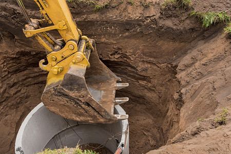 带铲斗的挖掘机，通过钢缆混凝土下水道环降入坑中。