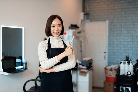 理发围裙摄影照片_一位年轻的亚洲女美发师拿着合格的理发工具的肖像。