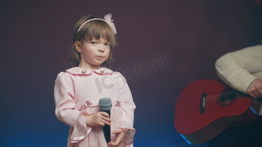 穿着粉色复古连衣裙的可爱小女孩站在舞台上，拿着麦克风