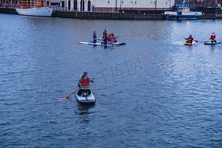 波兰格但斯克 2022 年 3 月，一群超级冲浪者站在桨板上，在老城黄昏的莫特拉瓦河和运河中一起划桨。