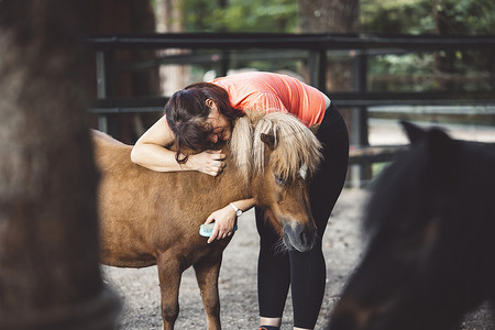 女人拥抱她的小马，给他梳理毛发，用刷子刷他的皮毛