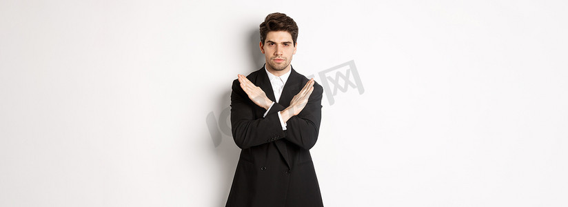 穿着黑色西装、严肃而关心的男人的肖像，表现出停止手势和皱眉，交叉禁止或拒绝某事，站在白色背景上