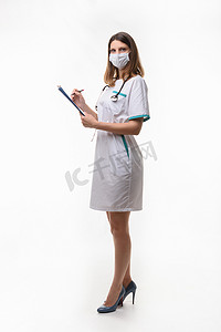 身着医用服装和医用口罩的苗条护士在白色背景下记录数据