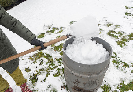 中年妇女正在用铲子在桶里收集雪，自然资源