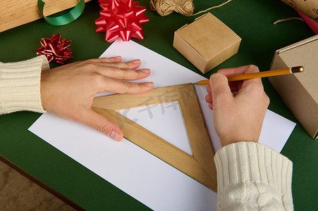 女人的手用尺子和木铅笔在白纸上画画，表面用包装材料包装礼品
