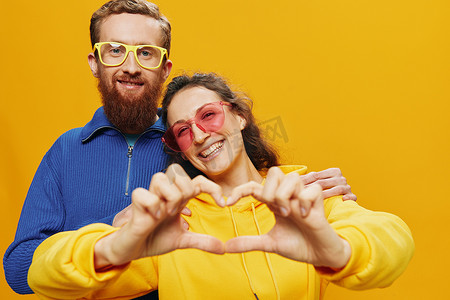 广告黄色摄影照片_男女情侣欢快地微笑着，戴着眼镜，在黄色背景上，符号标志和手势，家庭拍摄，新婚夫妇。