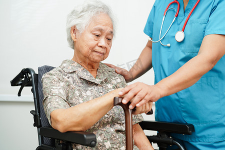 布满皱纹的手摄影照片_医生帮助亚洲老年残疾女患者在医院手握手杖，手上布满皱纹。