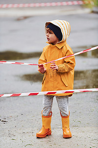 雨后穿着黄色防水斗篷和靴子的孩子在保护胶带附近户外玩耍
