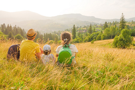 家属摄影照片_快乐的年轻家庭坐在后面看山家庭自然度假绿色旅行一起自然孩子山孩子父母孩子景观孩子。