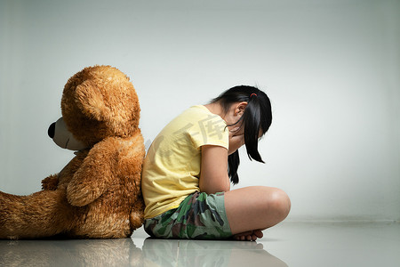 带着泰迪熊的小女孩坐在空荡荡的房间的地板上。