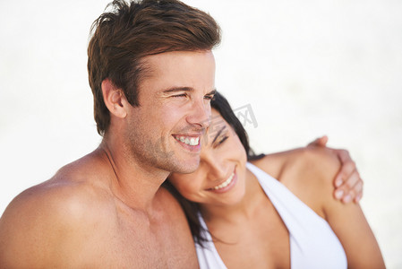 拥抱恩爱摄影照片_你是我唯一想要的……一对恩爱的年轻夫妇在海滩上互相拥抱，同时眺望地平线。