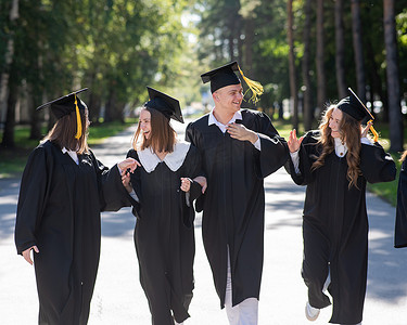 一排快乐的年轻人穿着毕业礼服在户外。